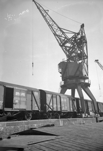 849770 Afbeelding van de overslag van goederen van trein naar schip in de haven te Rotterdam, met behulp van een havenkraan.